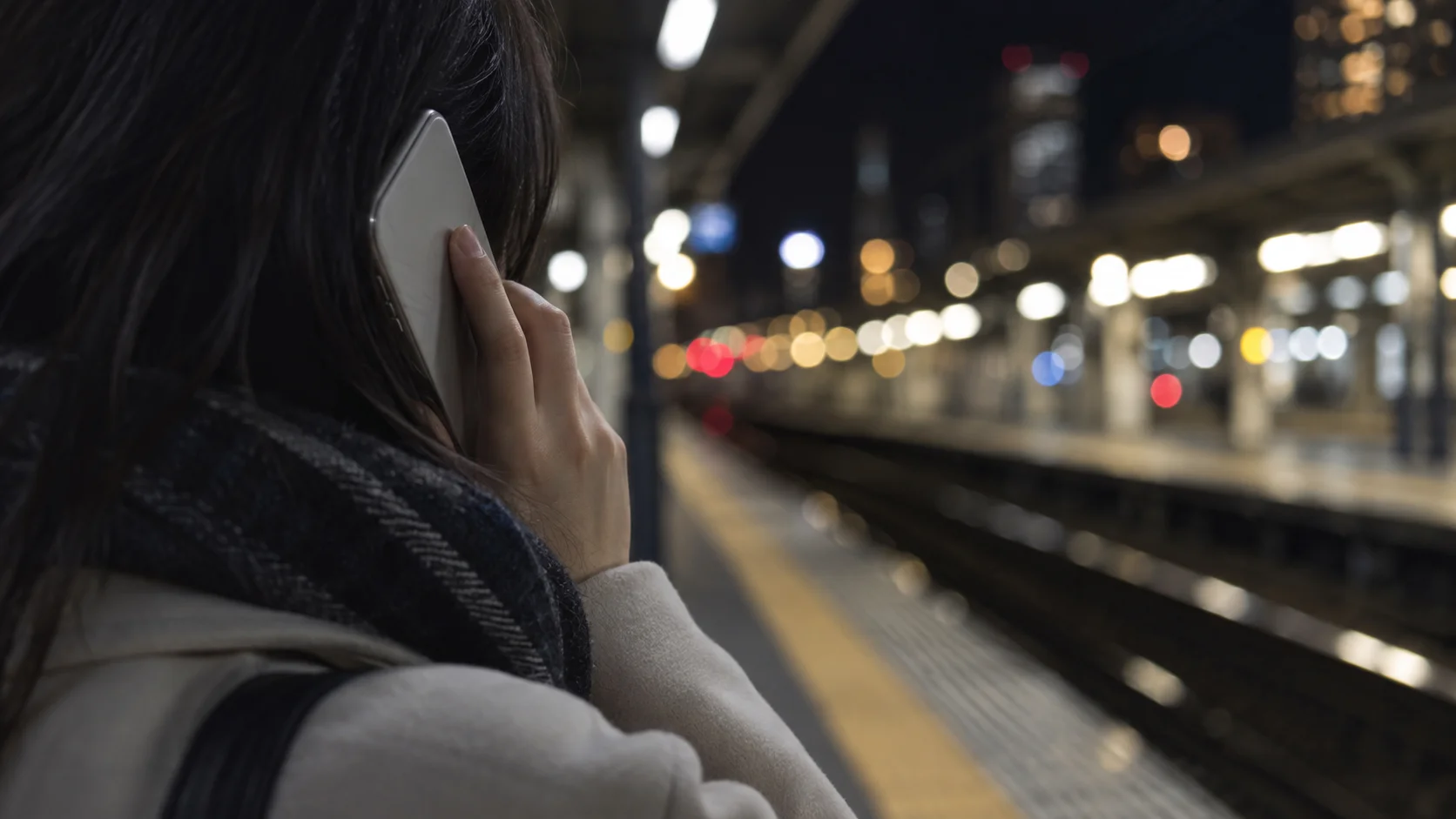 夜の駅のホームでスマートフォンを耳に当てる手元
